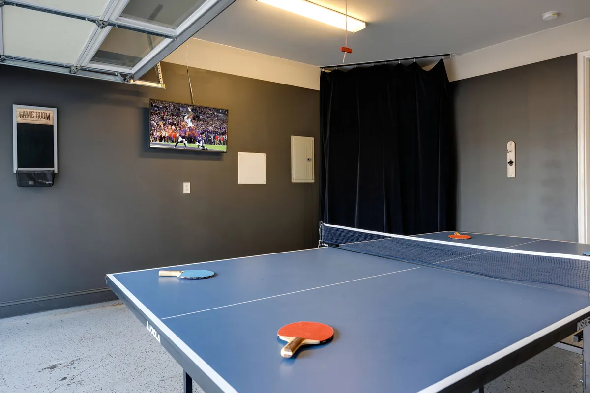 A lively interior featuring a ping pong table, a television mounted on the wall, and a sign indicating the room is dedicated to games. The space is designed for social activities, with plenty of room for movement and group play.