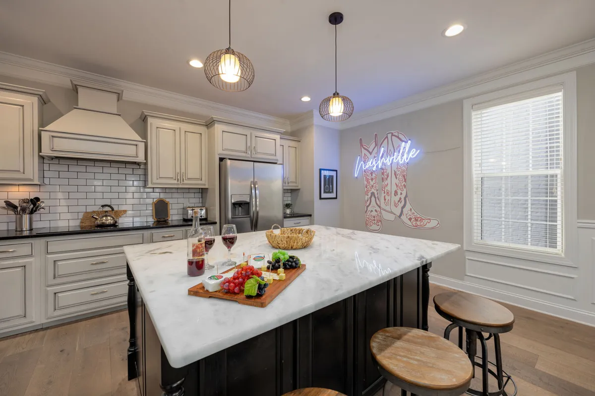 The kitchen is showcased with an oversized island topped with a charcuterie board, a playful neon 'Nashville' sign, and stylish pendant lighting. The inviting layout and décor highlight the space's modern amenities and its potential as a social hub for cooking and celebrating.