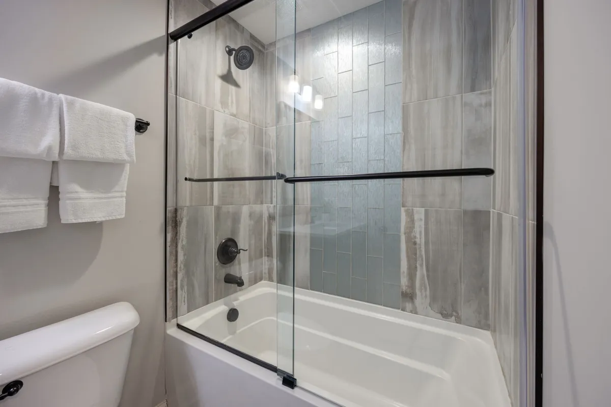A modern bathroom featuring a glass shower enclosure, textured tile detailing, and sleek fixtures. The design is tranquil and spa-inspired, setting the tone for a relaxing bath or shower experience.