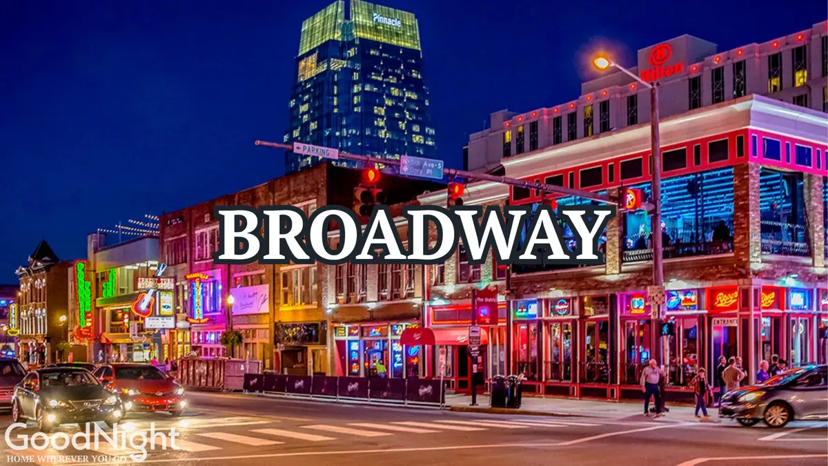 A bustling street lined with neon signs, colorful storefronts, a high-rise building, and people walking, dining, and shopping. The atmosphere is festive and lively, capturing the nightlife and social buzz of downtown Nashville.