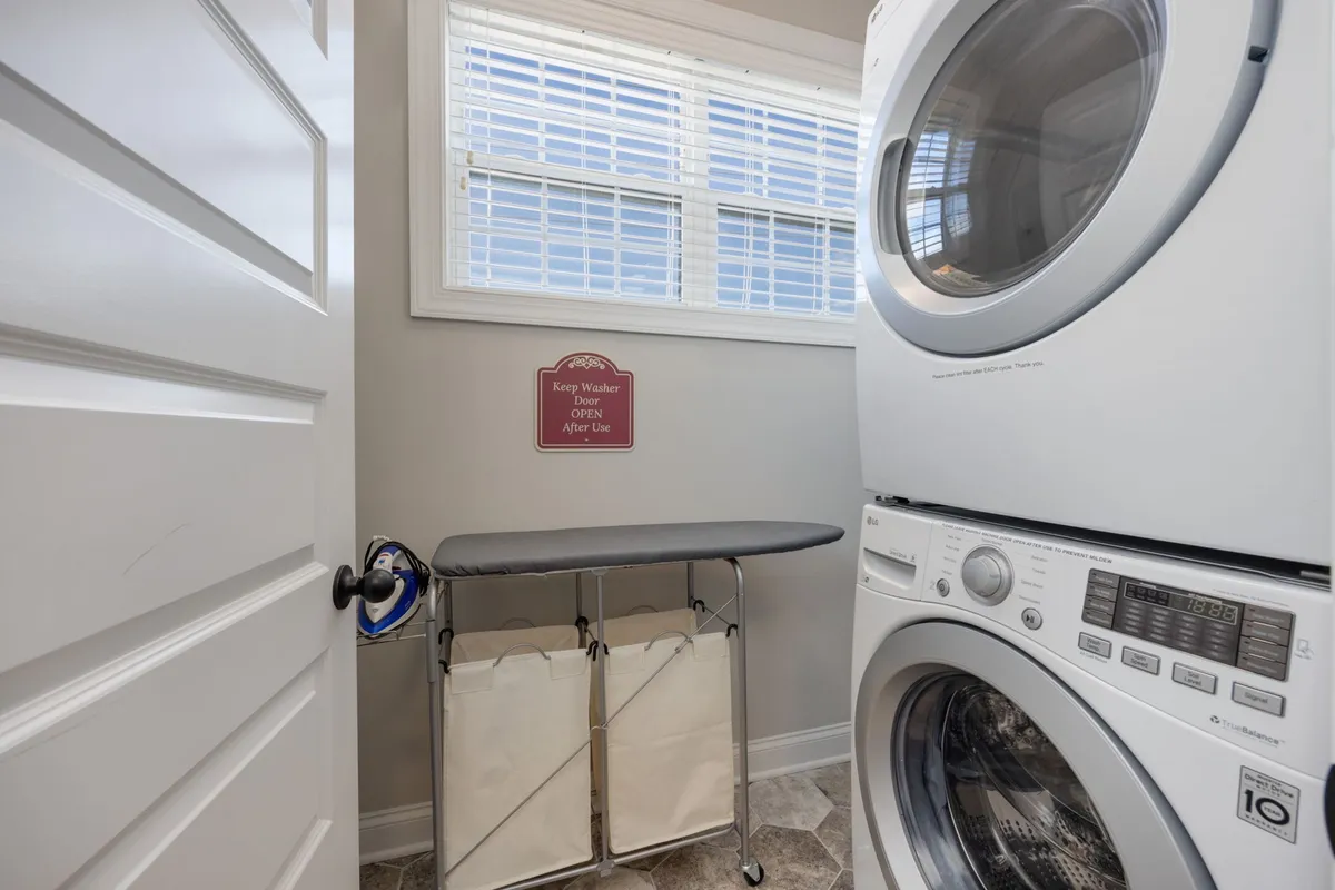 A well-equipped laundry area with a washer, dryer, ironing board, and laundry baskets, all bathed in natural light from a nearby window. The setup is organized and convenient for group stays.