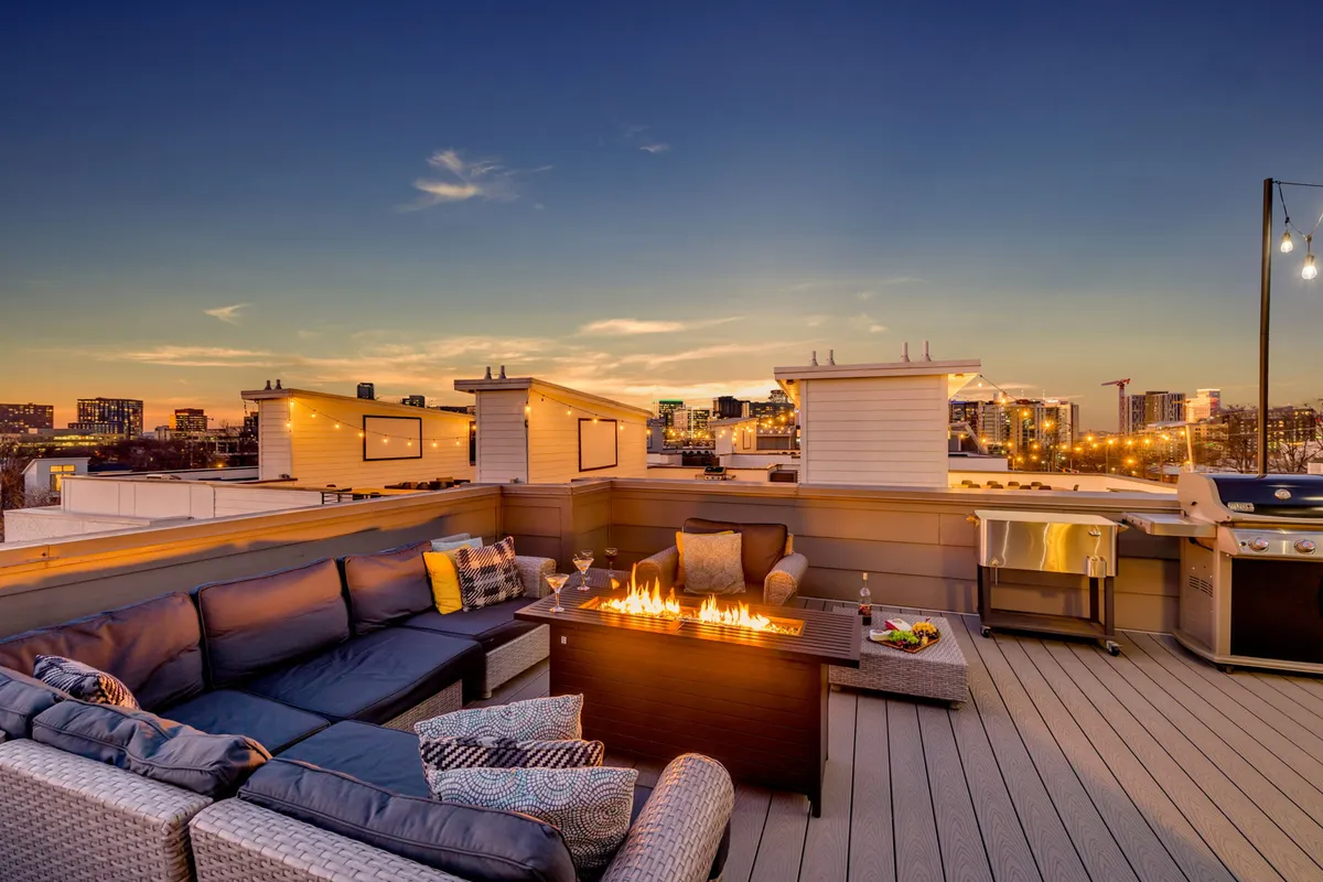 The hero image showcases the private rooftop terrace of the Gulch Melody townhome, featuring a cozy outdoor sofa arranged around a glowing fire pit, a modern grill for alfresco dining, and panoramic views of the Nashville city skyline. The warm lighting and inviting setup suggest a perfect spot for evening relaxation, social gatherings, or celebrating special occasions under the stars.