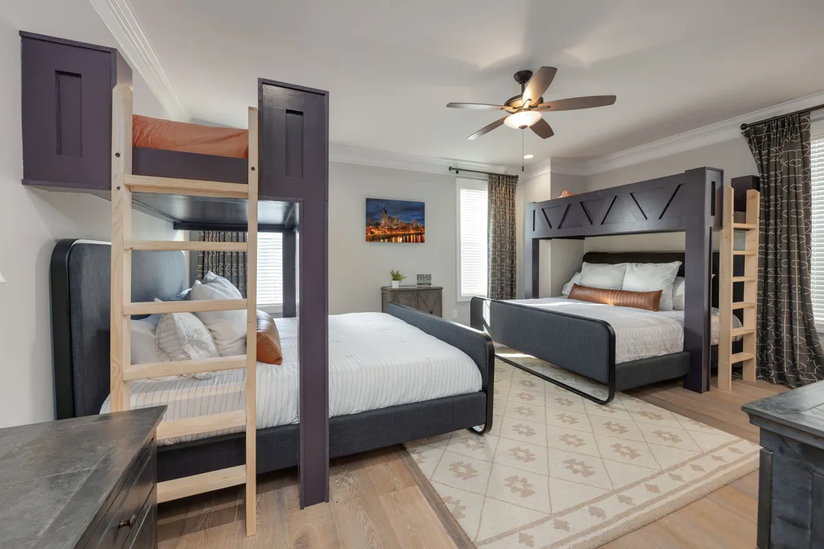 A spacious bedroom with multiple cozy bunk beds, complete with comfortable bedding and decorative pillows. A wooden ladder and playful artwork on the wall add a family-friendly, group-oriented feel.